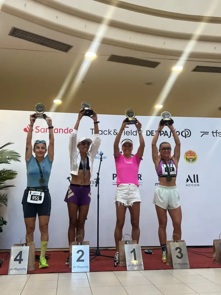 Carolina Carvalho, de camiseta rosa, ergue o troféu no degrau mais alto do pódio dos 21 km, ao lado de outras três corredoras