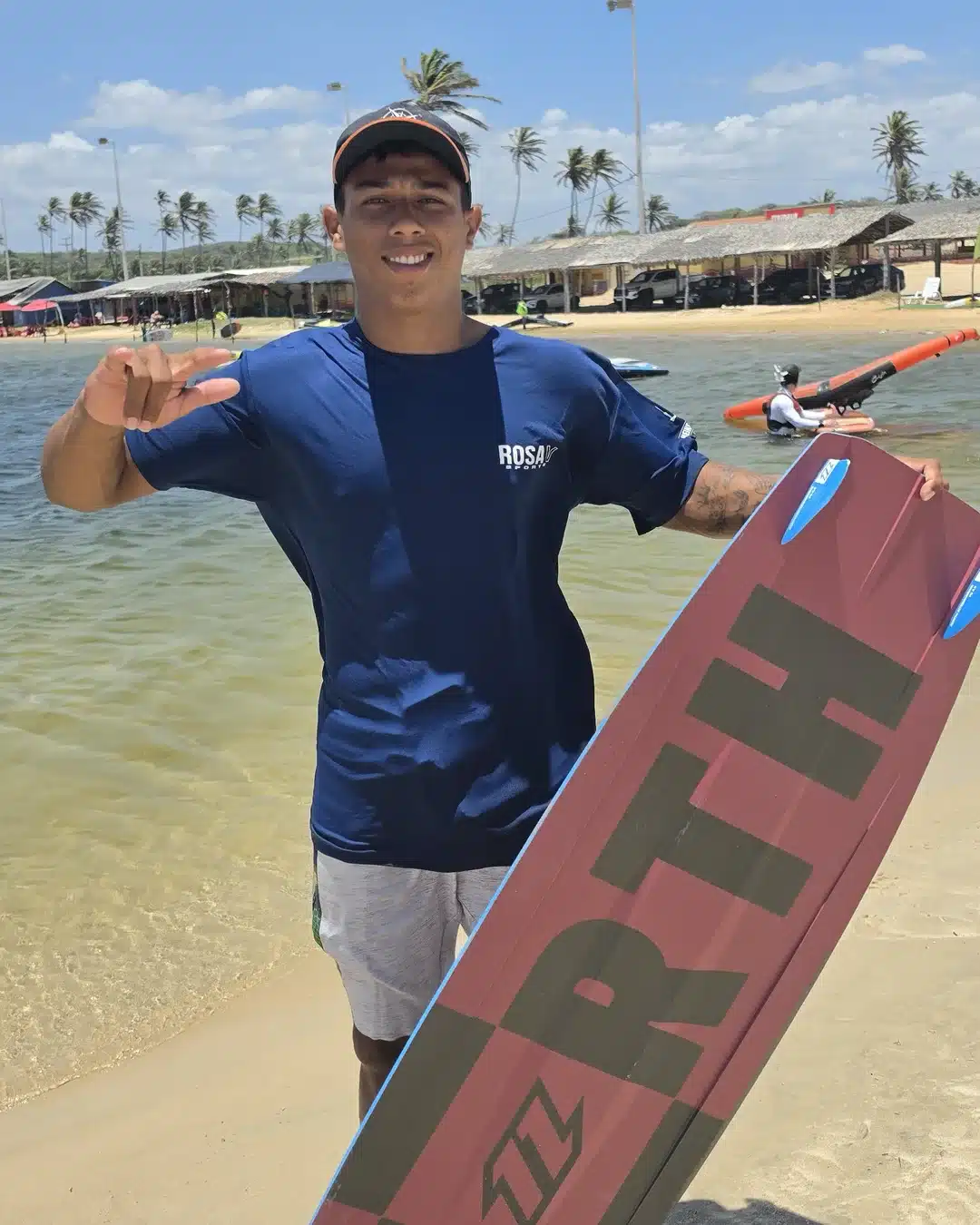 Mael, de camiseta azul da Rosa V, segura a prancha de kitesurf na areia da Lagoa do Cauípe